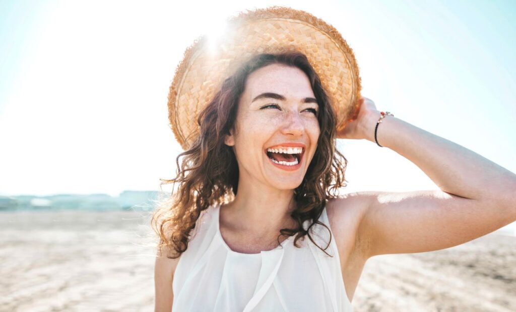 A woman in a sun hat smiling on the beach.