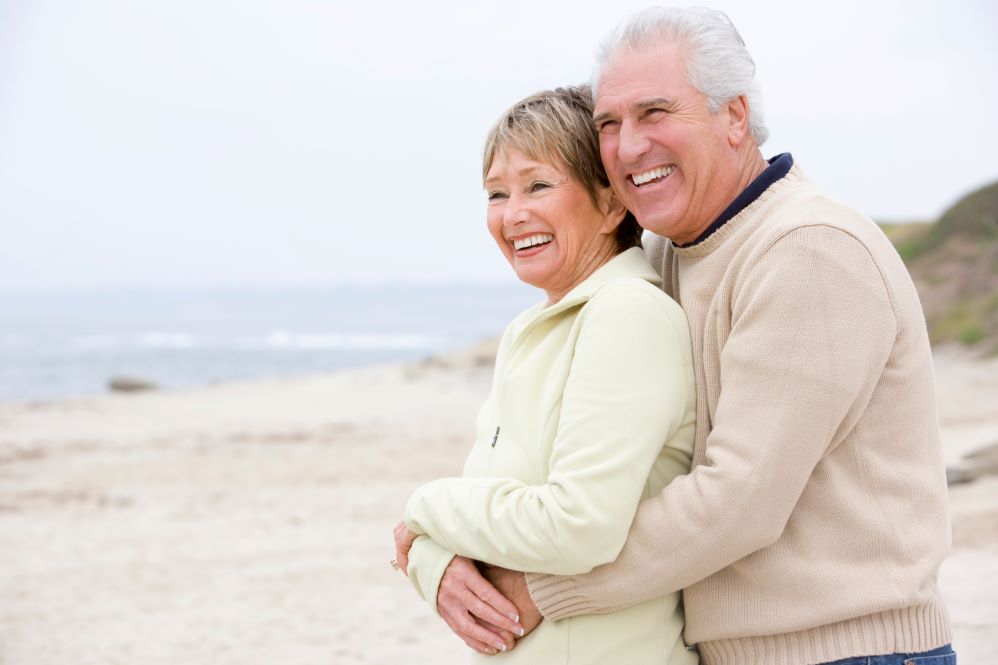 A mature couple hugging and smiling by the ocean.