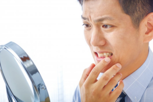 Man looking in mirror and wincing at his teeth